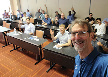 Image showing a CTS employee taking a selfie at a seminar with attendees waving in the background.