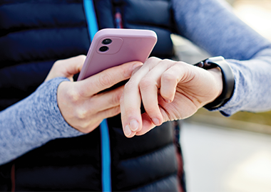 Woman in sports clothing looking at smartwatch and holding smart phone in her other hand, outdoors.