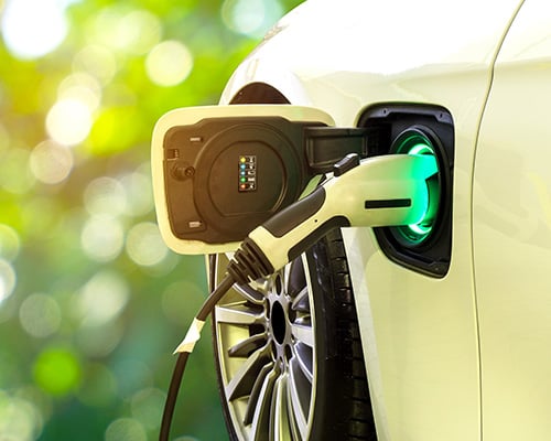 Electric car at charging station with the power cable plugged in on blurred nature with soft light background 
