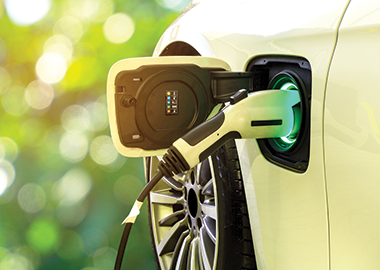 Electric car at charging station with the power cable plugged in on blurred nature with soft light background 