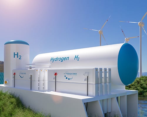 Image shows hydrogen storage tank, wind turbines and solar panels on the edge of a lake.