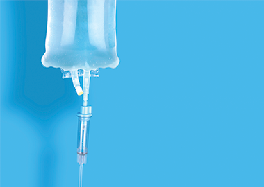 Hanging saline bag with syringe attached on bottom outlet on blue background.