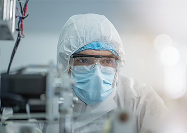 Man wearing mask, protective glasses and clothing working in a manufacturing cleanroom.