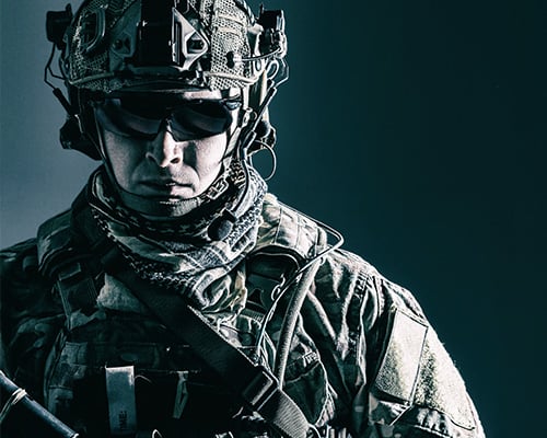 Male soldier wearing military tactical gear in front of dark background