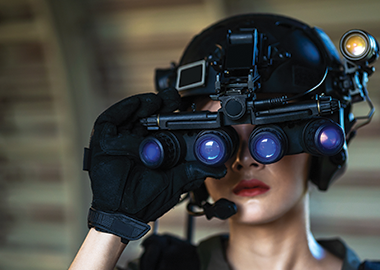 : Female soldier wearing helmet using four-eyed night vision goggles in dark background