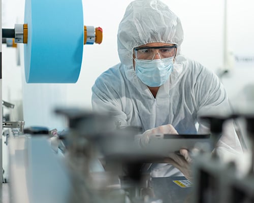 Man wearing mask, protective glasses and clothing working in a manufacturing cleanroom.