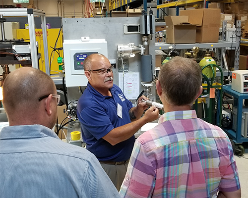 CTS employee in front of leak test machine talking to two men