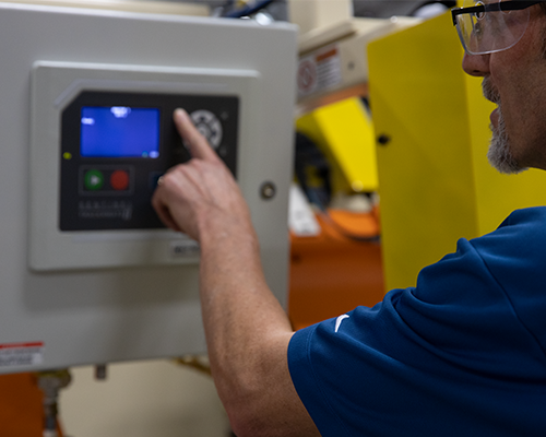 Side view of man in blue shirt looking up at and pushing buttons on a TracerMate II instrument.