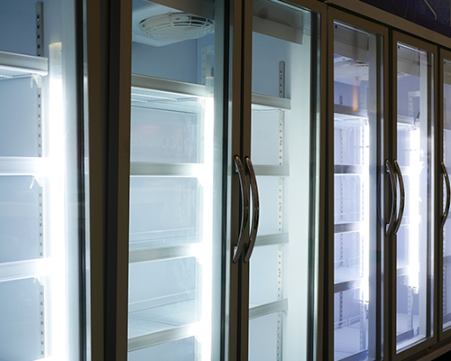 Close-up view of a large commercial refrigerator, with four full doors in center and white shelving inside.