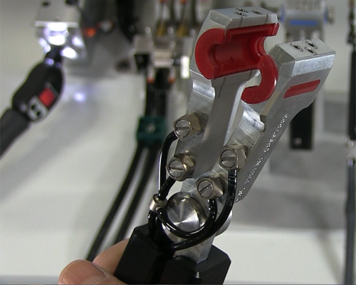 Close-up of a CTS nitrogen purge clamshell held open with a hand with the leak test fixture in the background.